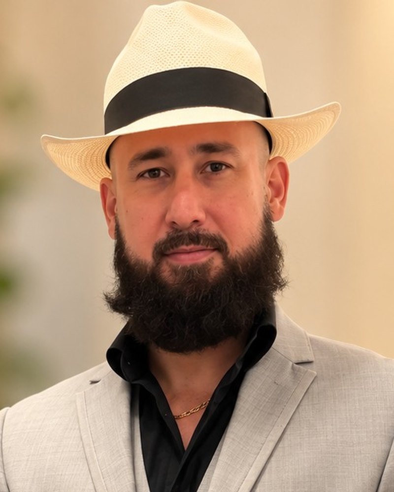 Professional portrait of Jhonantony Santana, Director of Latin America Operations of Remy's Consulting, wearing a light gray suit and a cream Panama hat against a softly blurred background